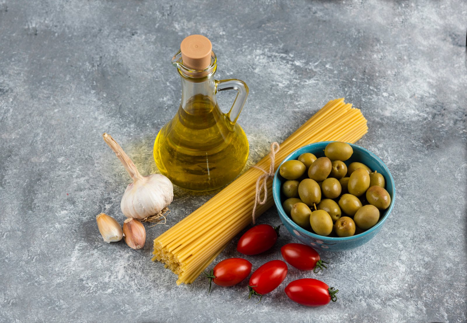 Uncooked pasta, oil and fresh vegetables on stone background. High quality photo